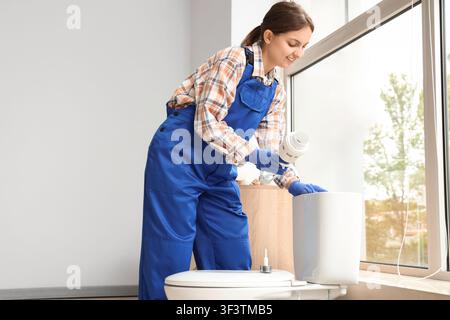 Idraulica in tute blu e guanti che installa un meccanismo di scarico del water in un bagno moderno, la lavoratrice qualificata è concentrata sul compito, assicurando Foto Stock