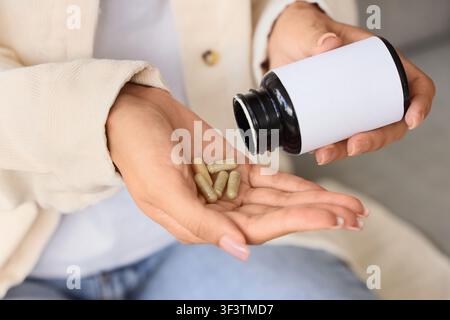 Mani di donna che versano capsule naturali di integratore a base di erbe da una bottiglia con etichetta bianca nel palmo della mano per la salute e il benessere quotidiani Foto Stock