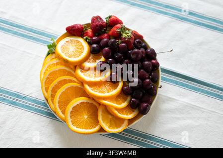 Un vassoio vivace con arance appena tagliate, ciliegie carnose e fragole mature disposte su un panno a righe. Perfetto per uno spuntino rinfrescante Foto Stock