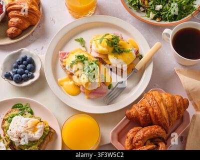 Una deliziosa tavola da brunch con uova alla benedict con salsa olandese, toast all'avocado, insalata di pesche grigliate e granola. Accompagnata da succo d'arancia e Foto Stock