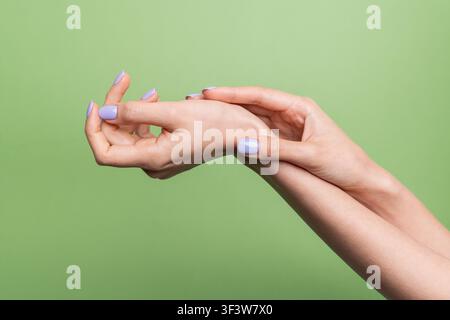 Close-up di mani di donna caucasica che fanno un gesto elegante con manicure lavanda pastello e pelle liscia, isolato su sfondo verde con spazio di copia Foto Stock