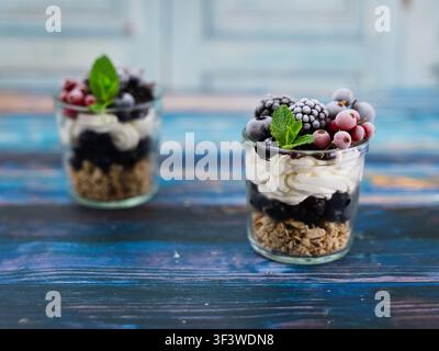 Composizione orizzontale con coppe di dessert allo yogurt, granola e frutti di bosco in stile rustico e luce naturale soffusa Foto Stock