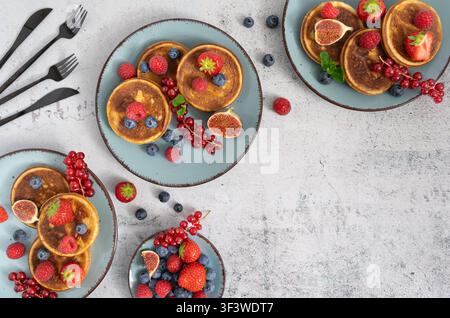Composizione brunch a vista dall'alto con pancake ricoperti di frutta disposti su uno sfondo texturizzato Foto Stock