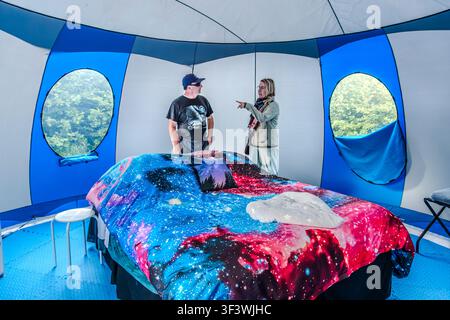All’interno di una tenda ‘Sky Bubble’ presso l’Osservatorio Deep Sky Eye vicino a Tusket, nella Nuova Scozia, l’ospite Timothy Doucette chiacchiera con Angela Berg davanti al letto, che è rifatto con lenzuola a tema galassia. Finestre trasparenti nella parete della tenda offrono una vista sugli alberi circostanti. Argyle Municipal, Nuova Scozia, Canada Foto Stock
