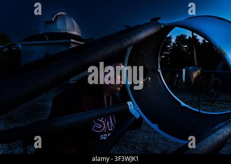 Un ricercatore junior guarda attraverso l'oculare di un grande telescopio Dobson sul terreno dell'Osservatorio Deep Sky Eye su Frotten Road nella municipalità di Argyle, Nuova Scozia, Canada. La cupola dell'osservatorio principale è visibile sullo sfondo Foto Stock
