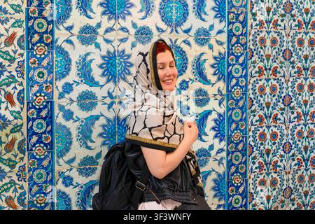 Istanbul, Turchia: 18 maggio 2026: Turista felice con foulard davanti alle piastrelle di Iznik nella moschea di Eyüpsultan Foto Stock