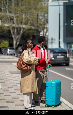 Allegra coppia sposata afroamericana di viaggiatori con bagagli in piedi sul marciapiede e che si guardano intorno. Foto Stock