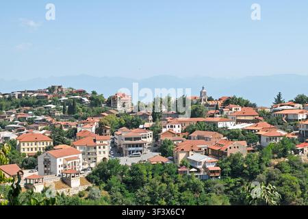 Ampia veduta aerea panoramica del paesaggio urbano di Sighnaghi con tetti di tegole, piazza centrale, torre campanaria, alberi verdi e montagne lontane in Kakheti Foto Stock