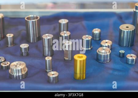 Prima vista di vari cilindri, ugelli e componenti industriali in metallo lavorati con precisione, disposti su un display in tessuto blu. Foto Stock