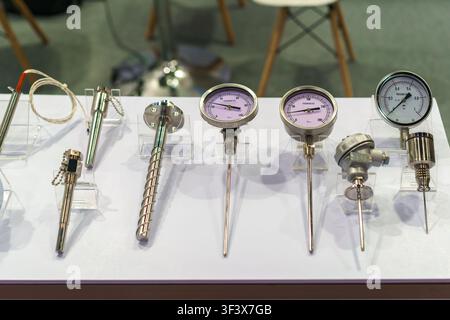 Prima vista di vari termometri bimetallici industriali, manometri e sensori di temperatura disposti su supporti in acrilico trasparente a un'esposizione Foto Stock