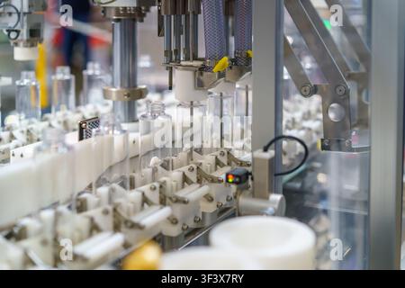 Primo piano di una macchina industriale automatizzata che elabora bottiglie di plastica trasparente su una linea di produzione moderna. L'attrezzatura utilizza ugelli precisi Foto Stock