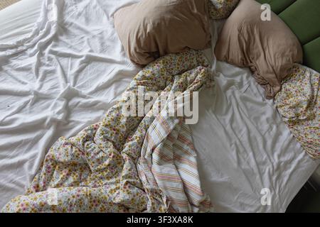Letto disordinato con coperte e cuscini in una camera da letto Foto Stock