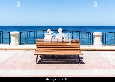Sliema, Malta – 19 maggio 2025: Una coppia di anziani siede su una panchina con vista sul calmo Mar Mediterraneo lungo la passeggiata di Sliema, godendosi una pacifica s Foto Stock