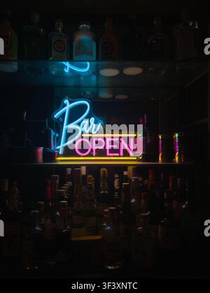 Insegna al neon "Aperto" per bar con bottiglie di liquore in un bar cocktail buio Foto Stock