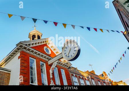 Orologio iconico della Borsa dei Cereali del XVII secolo che si estende sulla storica High Street di Rochester, Kent, UK, adornato da bandiere colorate sotto un cielo azzurro Foto Stock