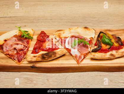 Quattro fette di pizza diverse con vari condimenti servite su una tavola di legno posizionata su uno sfondo di tavolo in legno. Foto Stock