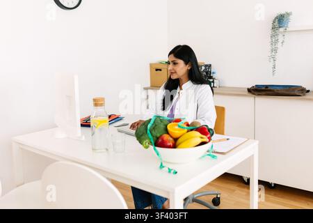 Dietista indiana che lavora al computer in un ufficio di nutrizione Foto Stock