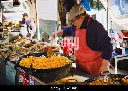 Un venditore di mercato che mescola patate cotte in una grande padella per paella a uno stand di street food ad Arles, in Francia. Foto Stock