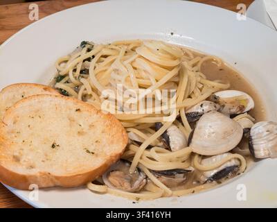 Una vista ravvicinata di spaghetti con vongole in una salsa cremosa serviti insieme a fette di pane all'aglio tostato in una ciotola bianca. Foto Stock