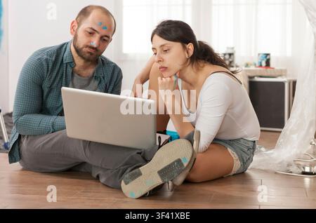 Coppia sposata che fa acquisti online per attrezzi per la ristrutturazione durante la ristrutturazione dell'appartamento, mostrando rulli per vernici, lavori di riparazione e miglioramento degli interni in un pratico restyling della casa. Foto Stock