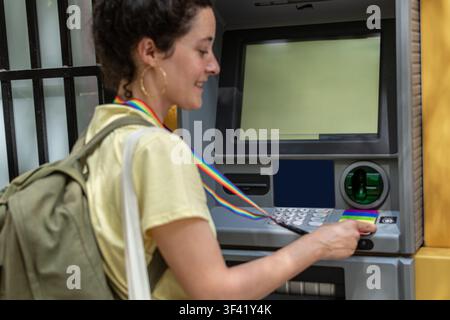 Donna che inserisce una carta di credito arcobaleno in un bancomat Foto Stock