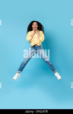 Giovane donna afroamericana felice che salta per l'entusiasmo, sfondo blu Foto Stock