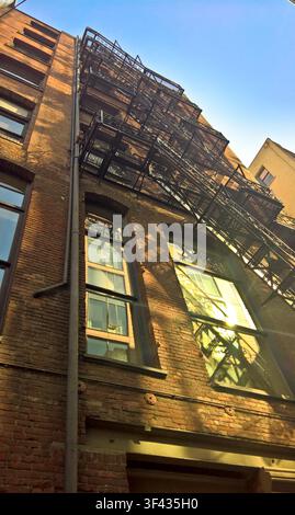 Edificio storico in mattoni con classica scala antincendio in ferro vista dal basso contro il cielo blu Foto Stock