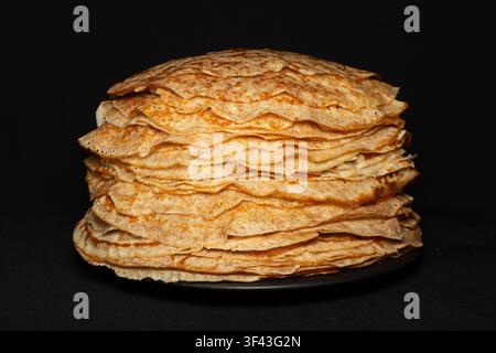 Una pila alta di pancake dorati e sottili appena sfornati serviti su uno sfondo scuro, perfetti per il menu della colazione. Foto Stock