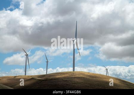 In un paesaggio sereno, alte turbine eoliche si ergono orgogliosamente su dolci colline, oscillando dolcemente con la brezza. L'atmosfera è luminosa, con nuvole che creano Foto Stock