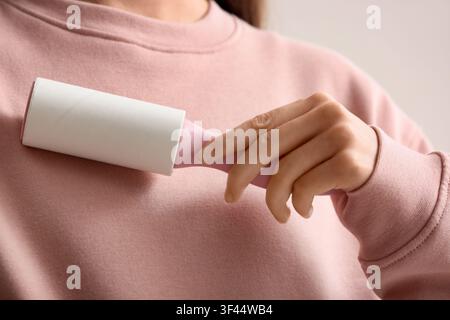 Donna che usa un rullo anti pelucchi su una felpa rosa, pulisce i vestiti e rimuove polvere e peli di animali Foto Stock