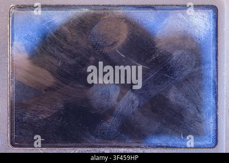 Vista ravvicinata dettagliata di uno schermo scuro all'interno di una cornice grigia strutturata. Numerose macchie e graffi creano motivi astratti, con accenni di blu e Foto Stock