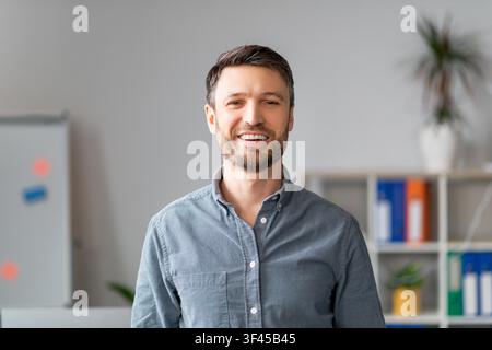 Giovane uomo caucasico sorridente in piedi in ufficio con atteggiamento professionale, concetto aziendale Foto Stock
