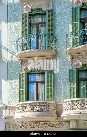 Barcellona - Spagna - 13 giugno 2026: Facciata di architettura modernista con persiane verdi, balconi fioriti, intagli ornamentali in pietra, edificio storico Foto Stock