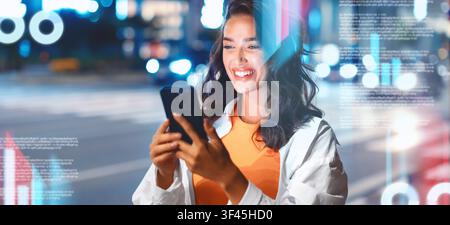 Giovane donna sorridente che usa lo smartphone di notte in città, concetto di connessione digitale Foto Stock