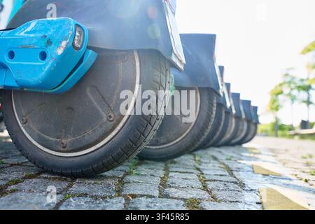 Ruote posteriori di scooter elettrici condivisi parcheggiati su una strada acciottolata. Concetto di trasporto urbano sostenibile Foto Stock