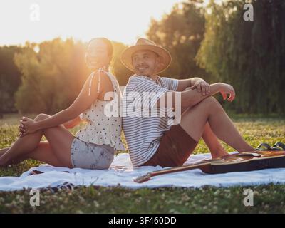 Una coppia allegra condivide un momento gioioso su una coperta da picnic circondata da una vegetazione lussureggiante al tramonto. Foto Stock