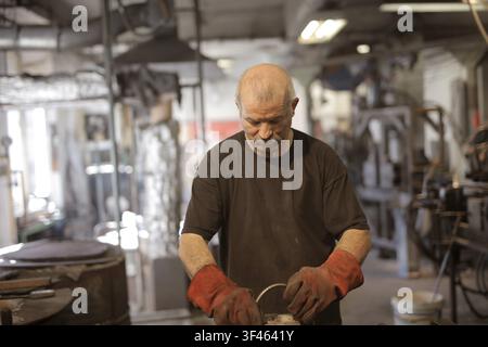 Artigiano anziano che lavora con il metallo nella sua officina Foto Stock