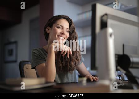 Giovane donna sorridente che lavora al computer a casa Foto Stock