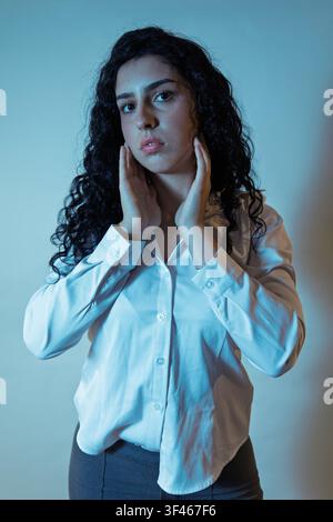 Donna con capelli ricci scuri che posa con le mani vicino al viso e un'espressione seria Foto Stock