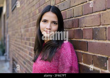 Giovane donna in maglione rosa si appoggia a un muro di mattoni Foto Stock
