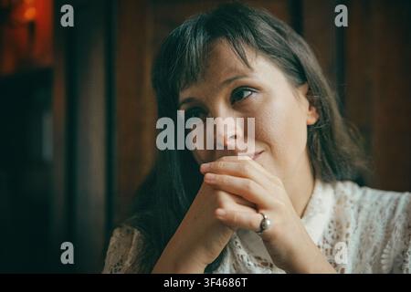 Donna pensierosa con le mani giunte sorride dolcemente Foto Stock