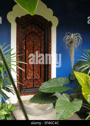 Affascinante porta in legno intagliata splendidamente artigianale nella mistica Bali tropicale. Casa indigo blu brillante a Ubud Foto Stock