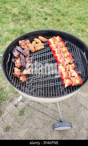 Barbecue rotondo con spiedini di shashlik e salsicce su carboni ardenti Foto Stock