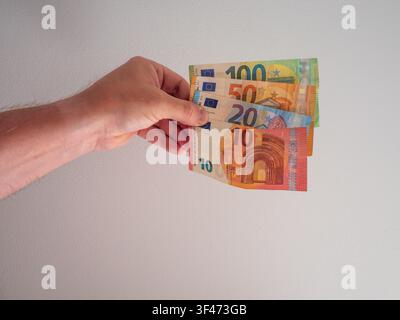 Prima piano di una mano che tiene un ventaglio di banconote in euro varie tra cui banconote da 10, 20, 50 e 100 euro su uno sfondo neutro chiaro. L'immagine Foto Stock