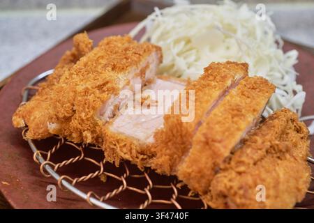 Cotoletta di maiale impanata a fette spesse con cavolo grattugiato su una griglia metallica che evidenzia l'autentica cucina gourmet asiatica e la cena al ristorante. Foto Stock