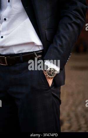 Uomo in completo blu scuro con orologio nero e cintura di pelle. Abbigliamento aziendale formale elegante, abito da sposo, stile di moda maschile di lusso Foto Stock