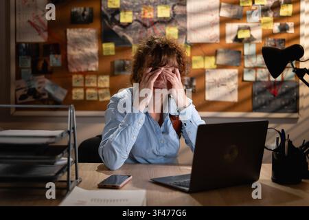 Criminologa seduta con il laptop, si strofina gli occhi, sente dolore e stanchezza per il sovraccarico di lavoro in ufficio di notte. Detective donna soffre di sindrome da ufficio. Concetto di Foto Stock