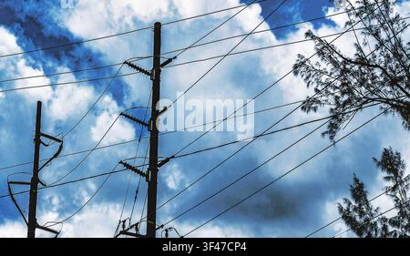 Linee elettriche e pali in legno sullo sfondo di un cielo blu e nuvoloso. Foto Stock