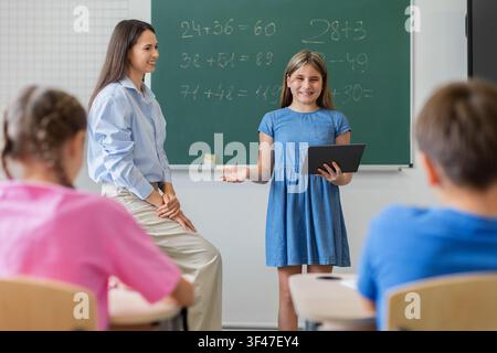 Studentessa sicura di sé che utilizza un tablet per presentare il lavoro di matematica ai compagni di classe Foto Stock