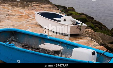 Barche a remi in legno blu e bianche tirate su un molo di granito, Portogallo Foto Stock